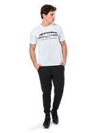 Alpinestars Prevail CSF Tee, koszulka z krótkim rękawem, biała, z logo z trzema kolorowymi paskami w stylu paddock i brandingiem Alpinestars z przodu, prezentowana na modelu w czarnych joggerach i czarnych sneakersach, codzienna moda uliczna w stylu motorsport