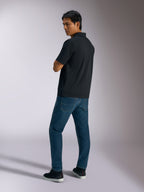 Alpinestars Impetus Sport Polo, czarna koszulka polo z krótkim rękawem o teksturze mesh i zapięciem na trzy guziki, noszona przez modela w niebieskich dżinsach i czarnych sneakersach, casualowy streetwear inspirowany sportami motorowymi