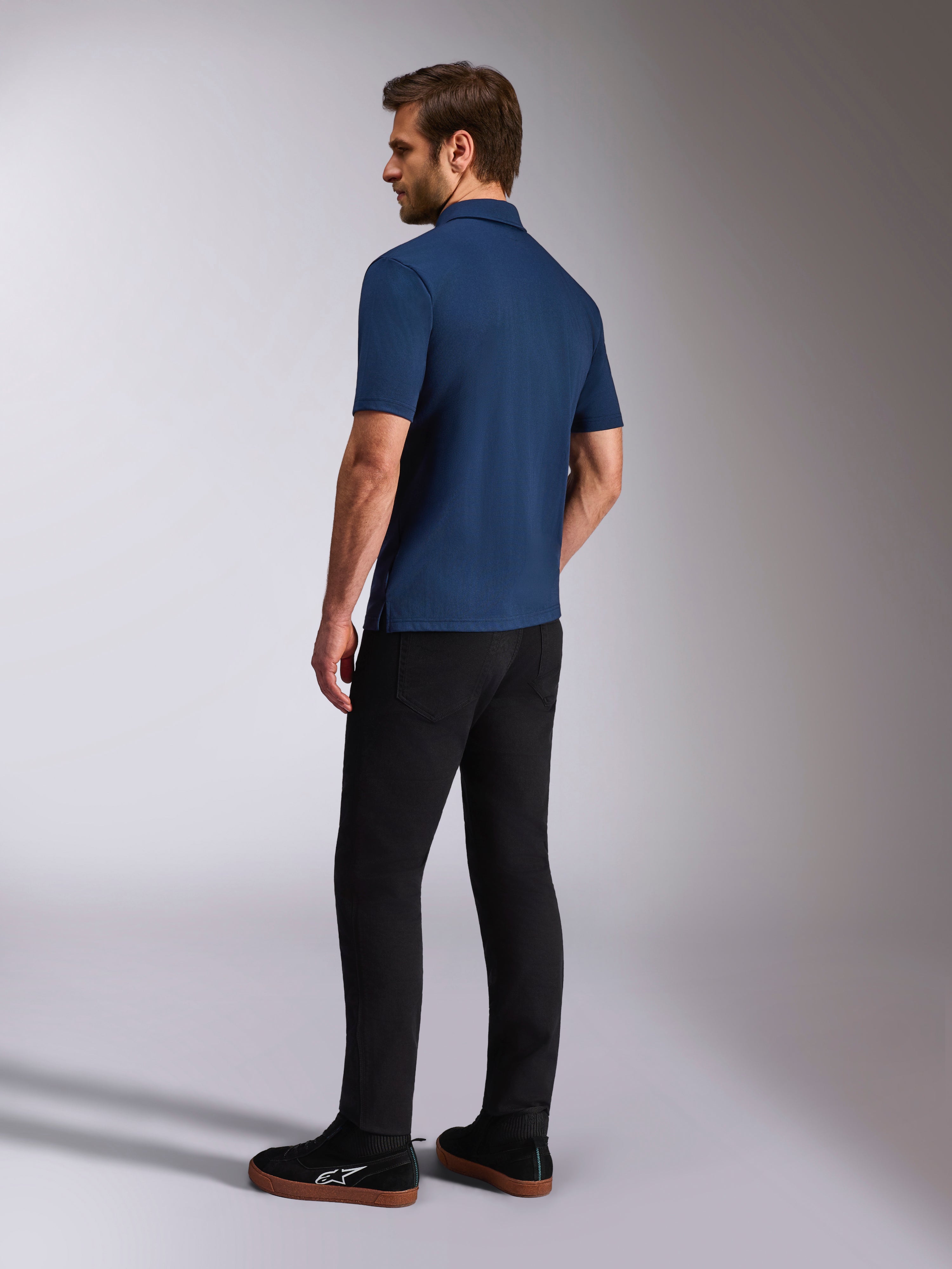 Alpinestars Impetus Sport Polo, Navy Blue Short Sleeve Polo Shirt, Back and side view on model, paired with black pants and black sneakers, casual motorsport lifestyle sportswear