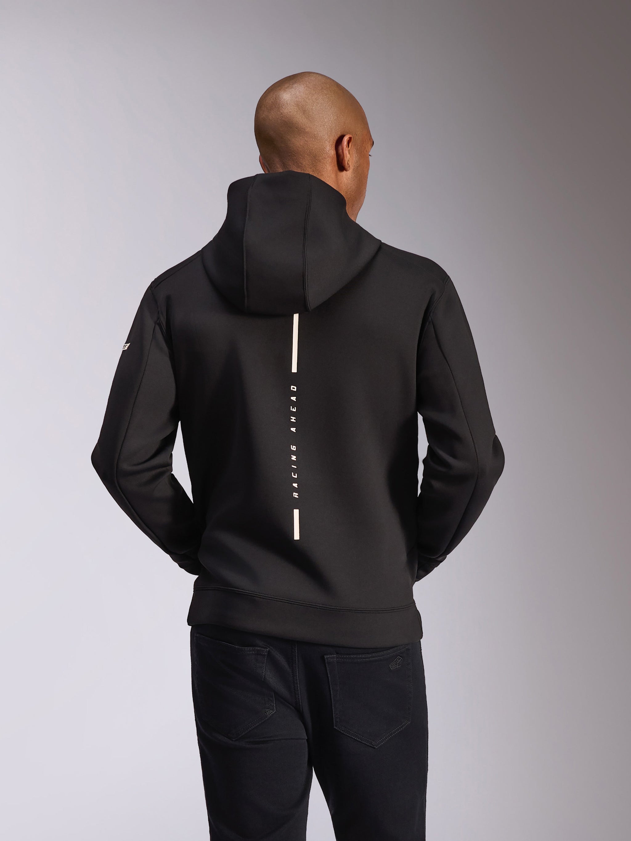 Alpinestars Insight Hoodie, widok z tyłu, czarna, pionowy biały pasek z napisem „RACING AHEAD”, logo na rękawie, codzienna odzież uliczna inspirowana sportami motorowymi
