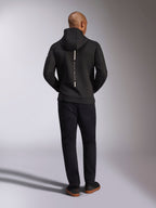 Alpinestars Insight Hoodie, czarna bluza z kapturem, widok z tyłu na modelu, pionowy biały pas z napisem „Racing Ahead” na plecach, sportowa bluza z dwustronnego polaru tri-blend, zestawiona z czarnymi spodniami