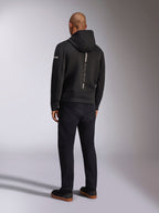 Alpinestars Insight Hoodie, czarna sportowa bluza z kapturem, widok z tyłu przedstawiający pionowy biały pasek z brandingiem „RACING AHEAD”, logo na rękawie, w zestawieniu z czarnymi spodniami i sneakersami, casualowy design inspirowany sportami motorowymi