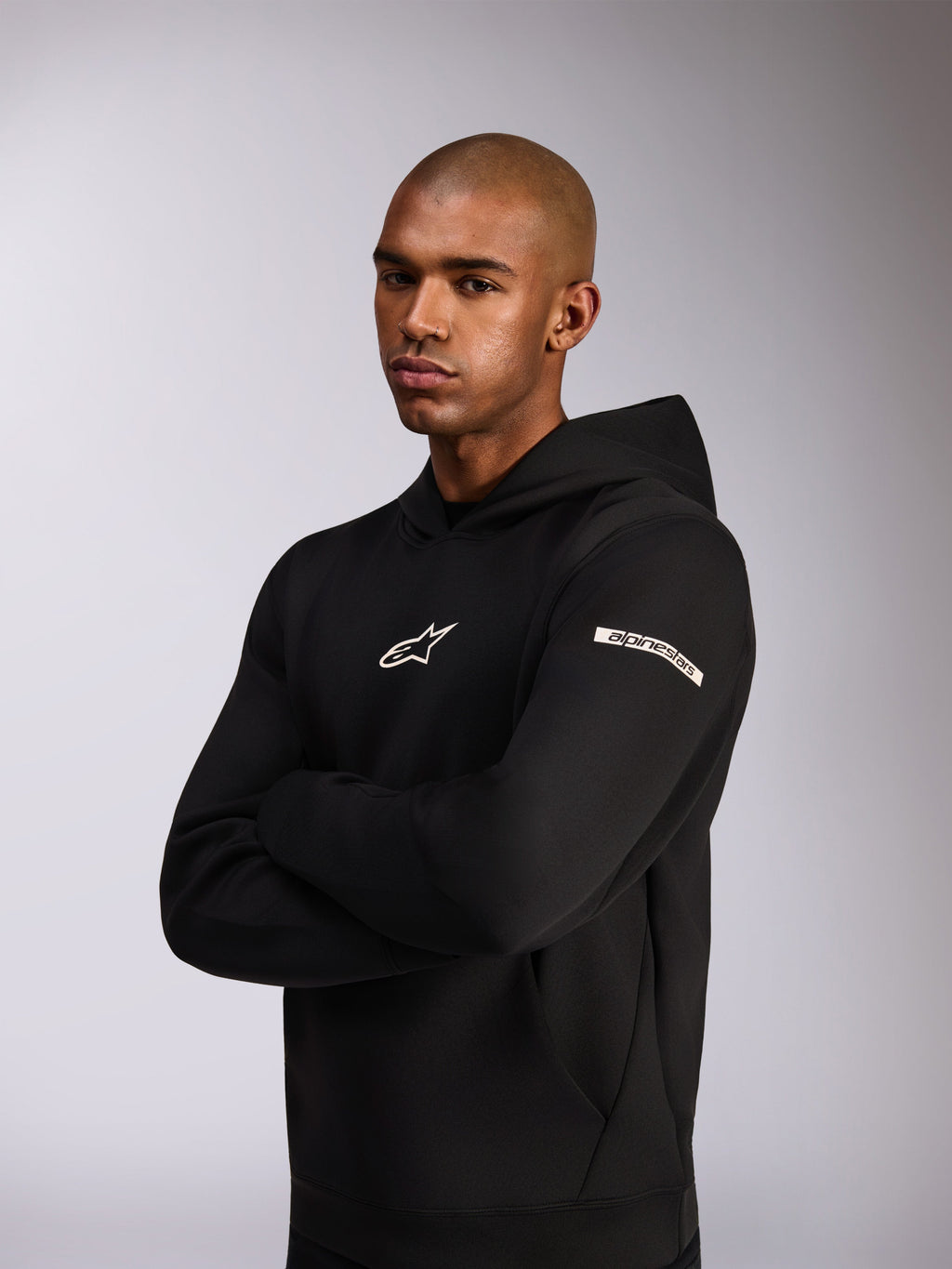 Alpinestars Insight Hoodie, sportowa bluza z kapturem, czarna, białe logo Astars na piersi i logo z napisem na górnym rękawie, model w bluzie ze skrzyżowanymi rękami, konstrukcja z wysokiej jakości dwustronnego polaru