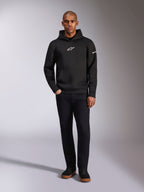 Alpinestars Insight Hoodie, czarna bluza z kapturem typu pullover z białym logo Astars na piersi i rękawie, prezentowana na modelu w czarnych spodniach i czarnych sneakersach, casualowy streetwear inspirowany motorsportem