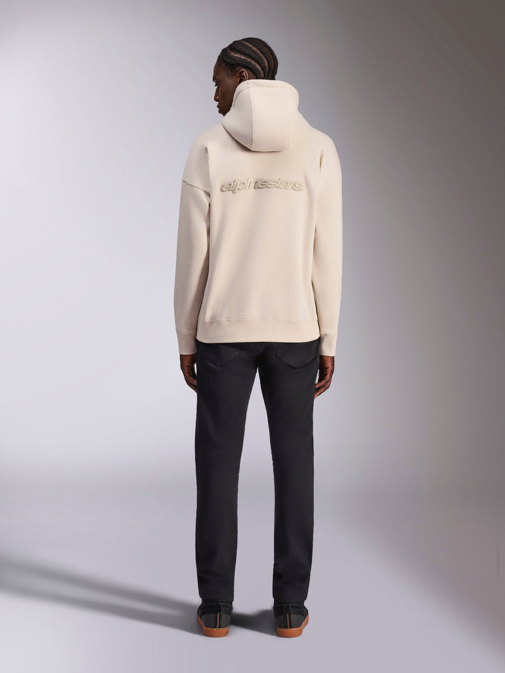 Alpinestars Emergent Oversized Hoodie, kolor Off White, widok od tyłu z haftowanym logotypem 3D Alpinestars, polarowa bluza o kroju oversize, zestawiona z czarnymi spodniami, streetwearowy styl