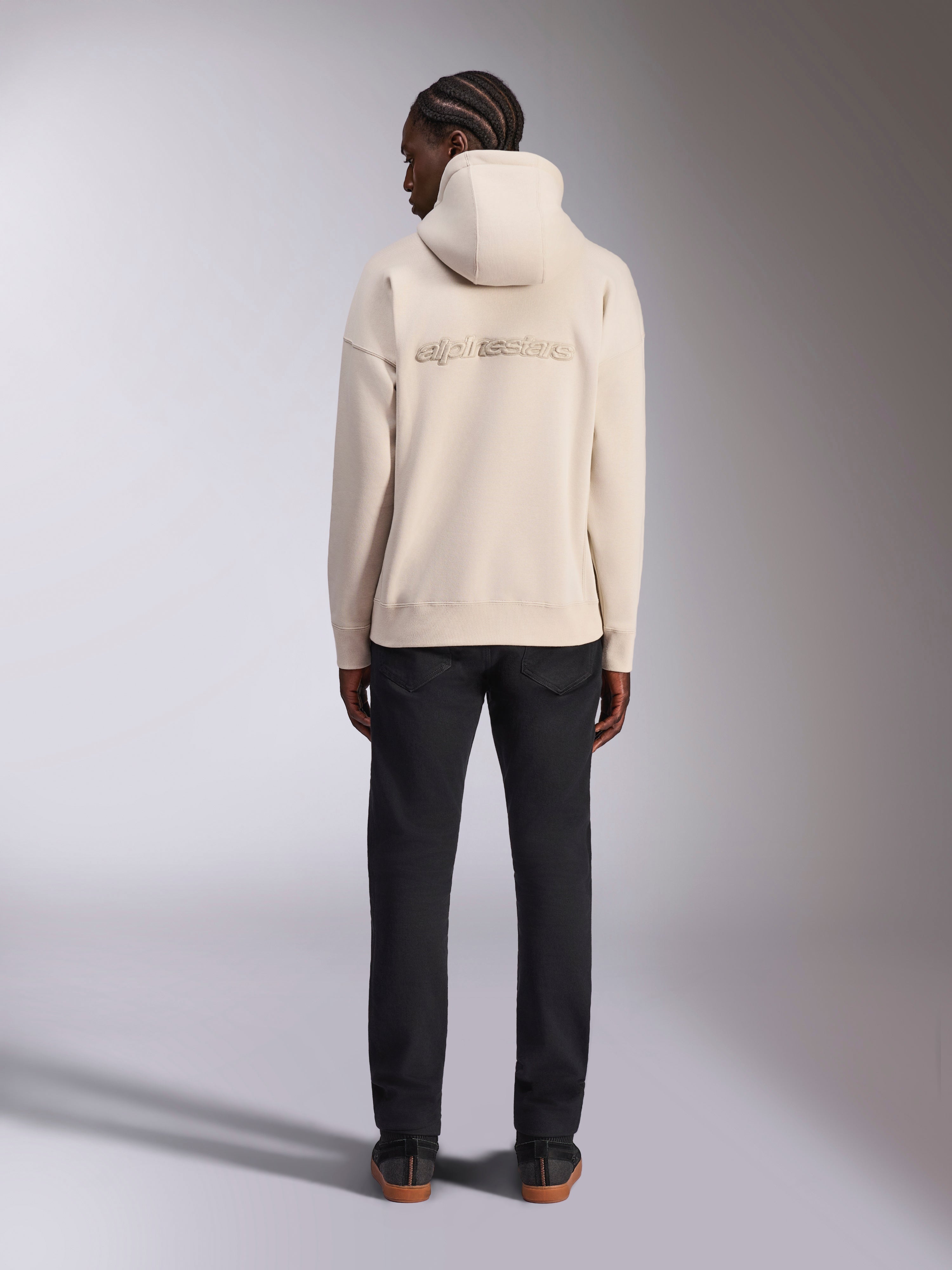 Alpinestars Emergent Oversized Hoodie, kolor Off White, widok od tyłu z haftowanym logotypem 3D Alpinestars, polarowa bluza o kroju oversize, zestawiona z czarnymi spodniami, streetwearowy styl