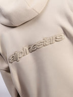 Alpinestars Emergent Oversized Hoodie, casual streetwear, kolor piaskowy, zbliżenie na tonalne haftowane logo 3D Alpinestars na plecach, tekstura polaru premium
