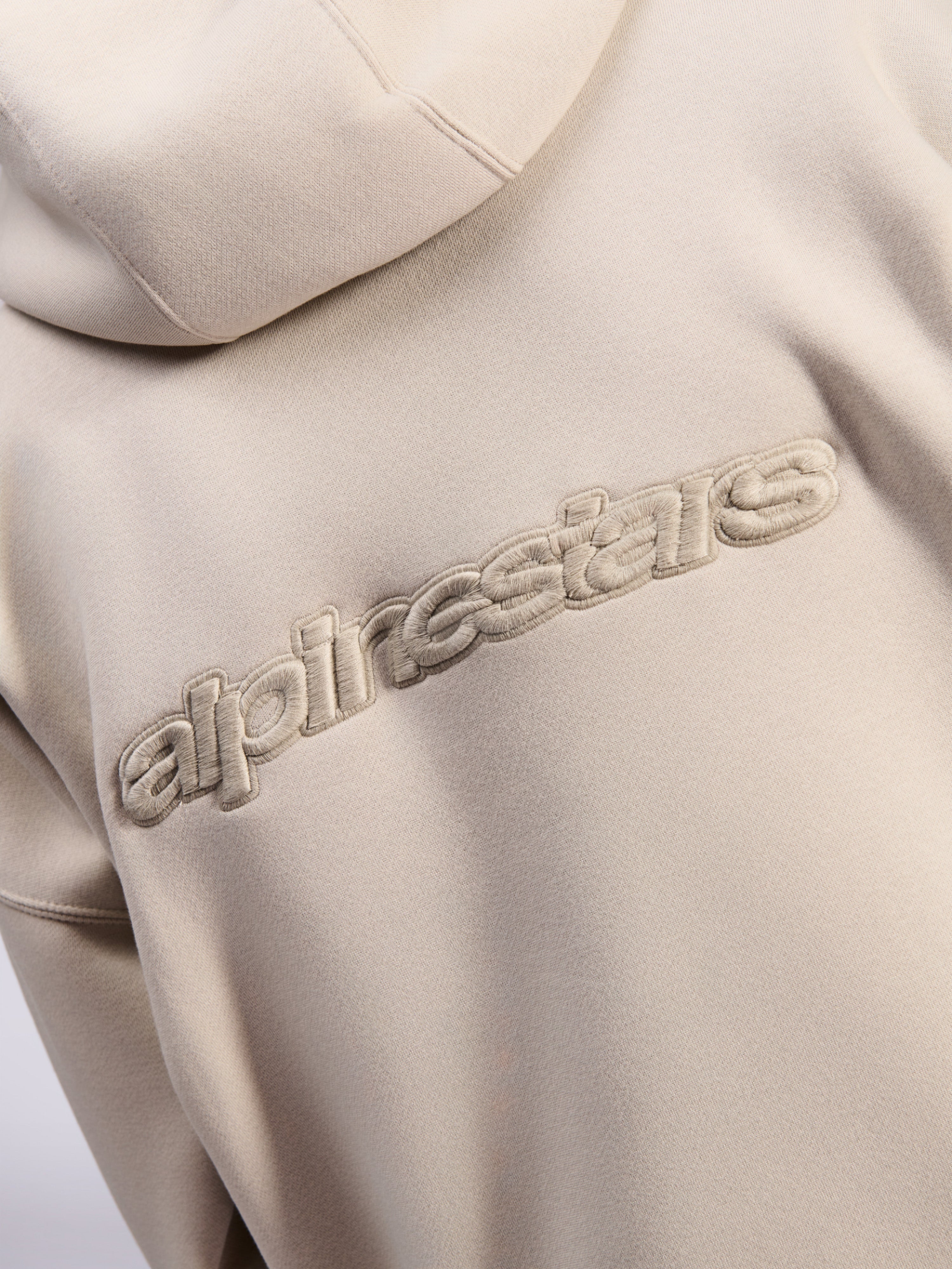 Alpinestars Emergent Oversized Hoodie, casual streetwear, kolor piaskowy, zbliżenie na tonalne haftowane logo 3D Alpinestars na plecach, tekstura polaru premium