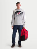 Alpinestars Bluza z kapturem Obsessed, męska bluza polarowa sportswear, szara z czerwono-czarną grafiką inspirowaną MX, logo na rękawach, model trzymający czerwony plecak Alpinestars.