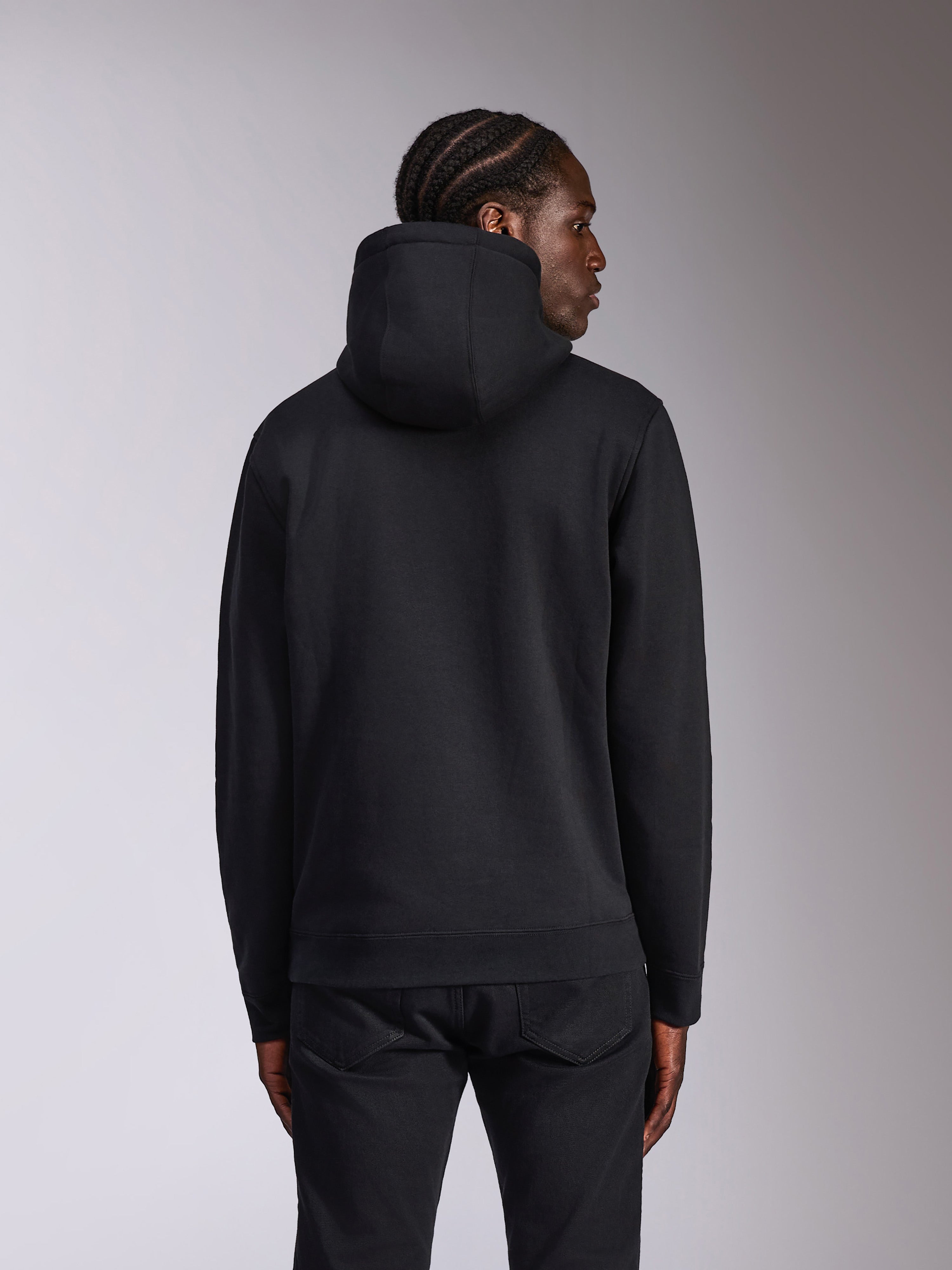 Alpinestars Pulse Hoodie, czarna, widok z tyłu na modelu, codzienna odzież typu streetwear, polarowa bluza z kapturem o jednolitym czarnym designie, prążkowane ściągacze na mankietach i na dole, zestawiona z czarnymi spodniami
