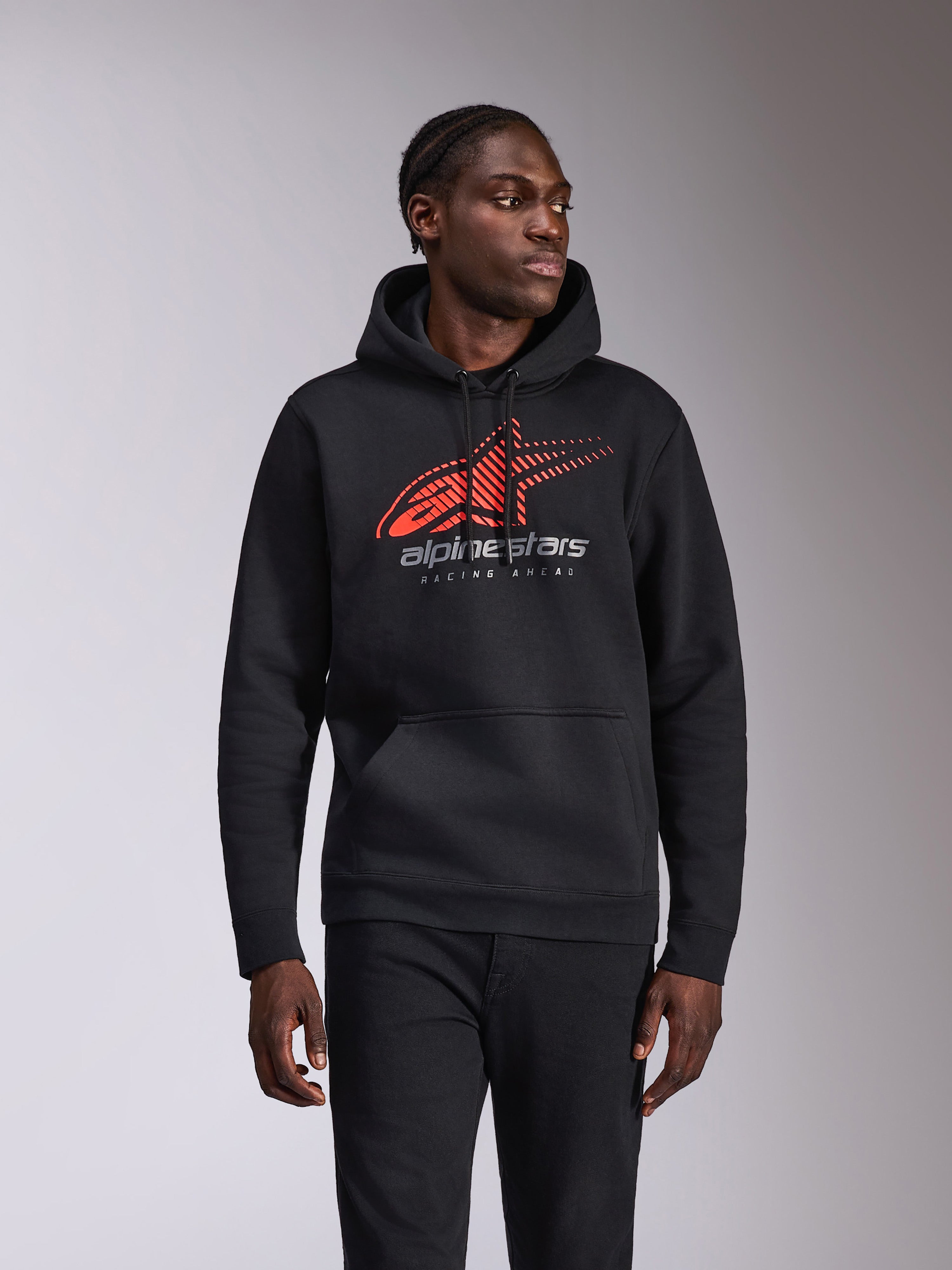 Alpinestars Pulse Hoodie, codzienna bluza z kapturem typu pullover, czarna z czerwono-szarym logo Astars z efektem przejścia i liniami prędkości oraz napisem „Racing Ahead”, kaptur ze sznurkiem i kieszeń typu kangurka, streetwear inspirowany motorsportem prezentowany na modelu