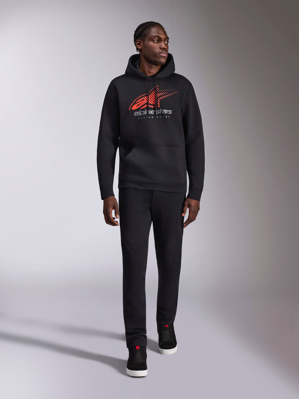 Alpinestars Pulse Hoodie, czarna casualowa bluza streetwear z kapturem, czerwono-szare logo Astars combo z efektem linii prędkości na klatce piersiowej, kaptur ze sznurkiem, przednia kieszeń typu kangurka, długie rękawy, zestawiona z czarnymi spodniami i sneakersami, design inspirowany motorsportem