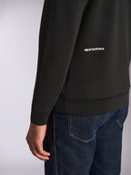 Alpinestars Cypher Hoodie, zbliżenie na dolną część pleców i rękaw, czarny dwustronny polar z białym logotypem Alpinestars, noszona z niebieskimi jeansami, codzienna odzież streetwearowa w stylu motorsport