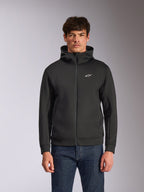 Alpinestars Cypher Hoodie, czarna rozpinana bluza z kapturem z polaru, wysoki kołnierz z białym brandingiem i małe białe logo Astars na piersi, prezentowana przez modela w niebieskich jeansach, codzienna odzież streetwear inspirowana motorsportem.