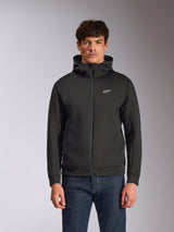Alpinestars Cypher Hoodie, czarna rozpinana bluza z kapturem z polaru, wysoki kołnierz z białym brandingiem i małe białe logo Astars na piersi, prezentowana przez modela w niebieskich jeansach, codzienna odzież streetwear inspirowana motorsportem.