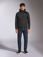Model w bluzie Alpinestars Cypher Hoodie, czarna rozpinana bluza z polaru, wysoki kaptur z małym białym logo Astars na piersi, ciemne jeansy i czarne sneakersy, casualowy streetwear inspirowany motorsportem