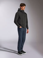 Alpinestars Cypher Hoodie, casual streetwear, czarna bluza z kapturem zapinana na zamek, męski model ubrany w ciemnoniebieskie dżinsy i czarne sneakersy, wysoki kaptur z logotypem Alpinestars, małe białe logo Astars na piersi, stylowy wygląd lifestylowy inspirowany sportami motorowymi