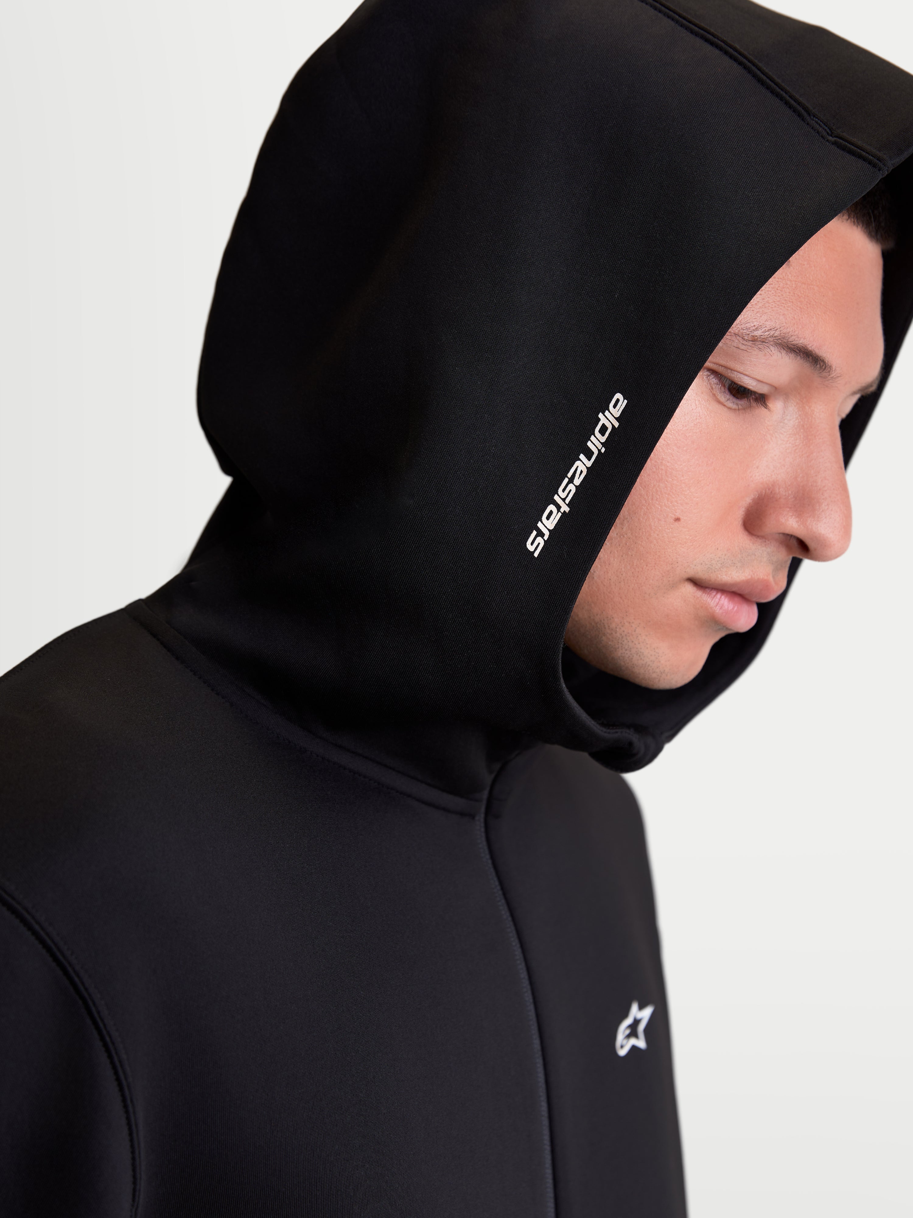 Alpinestars Cypher Hoodie, męska sportowa bluza z kapturem, czarna, zbliżenie na modela pokazujące wysoki kaptur z białym logo Alpinestars i techniczny polar tri-blend