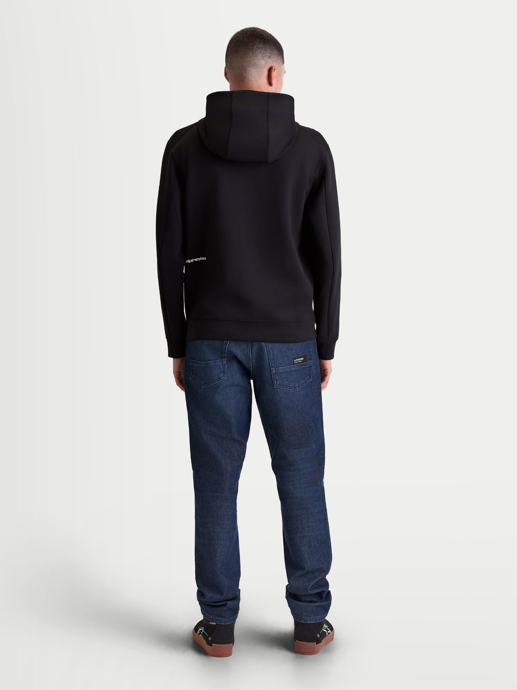 Alpinestars Cypher Hoodie, czarna sportowa bluza z kapturem z polaru, widok od tyłu na modelu przedstawiający wysoki kaptur i minimalistyczne logo, materiał tri-blend, casualowa odzież streetwearowa i styl życia motorsport.