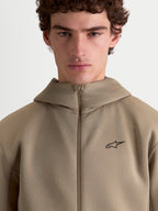Alpinestars bluza z kapturem Cypher, beżowa sportowa bluza z wysokim kapturem prezentowana na modelu, pełny zamek, małe czarne logo Alpinestars na piersi, techniczna tkanina tri-blend, codzienna odzież sportowa