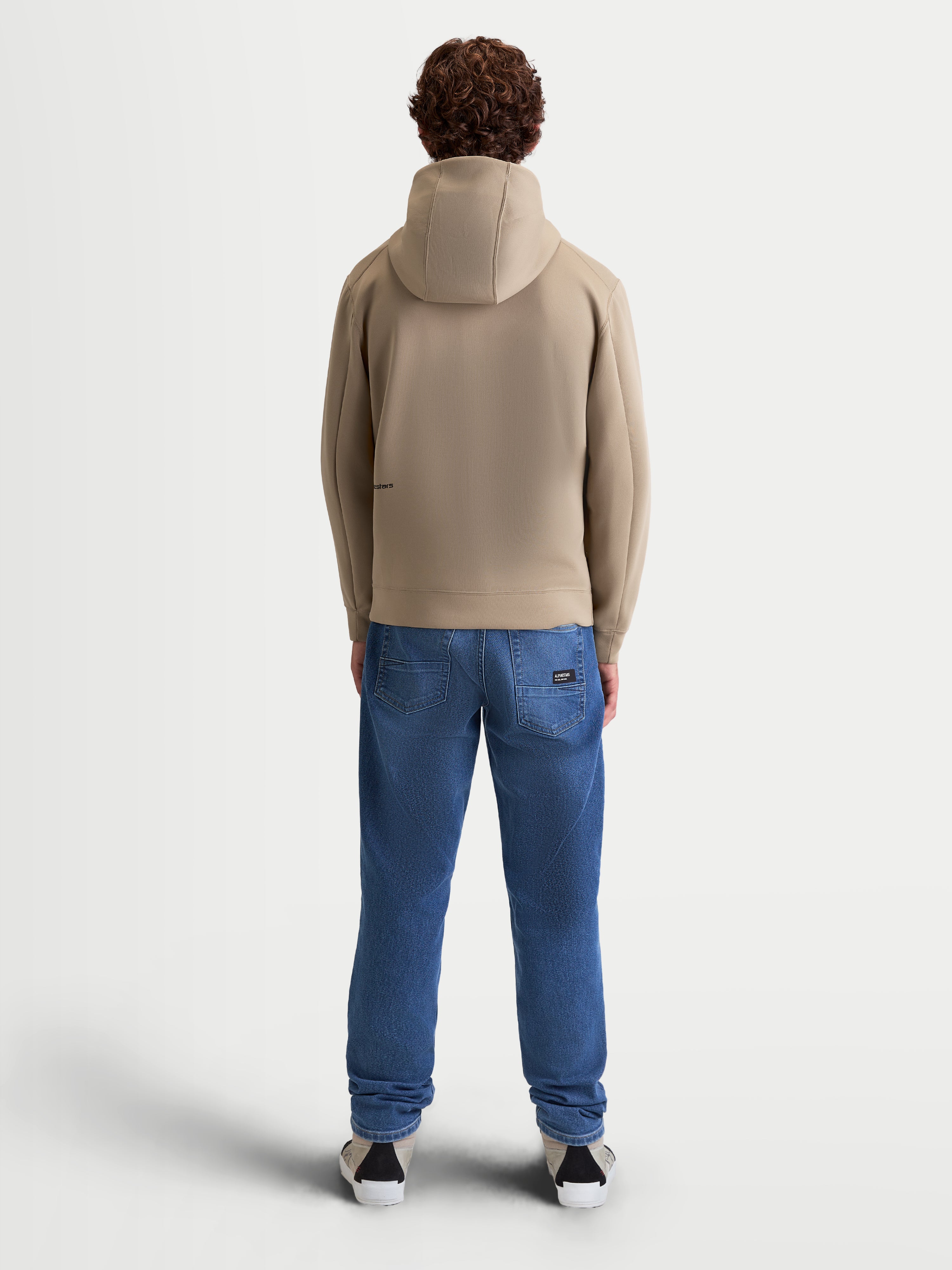 Alpinestars bluza z kapturem Cypher, sportowa bluza z polarem, beżowa, widok od tyłu na modelu, wysoki kaptur z siatkową podszewką, techniczna tkanina tri-blend, casualowa odzież sportowa inspirowana motorsportem
