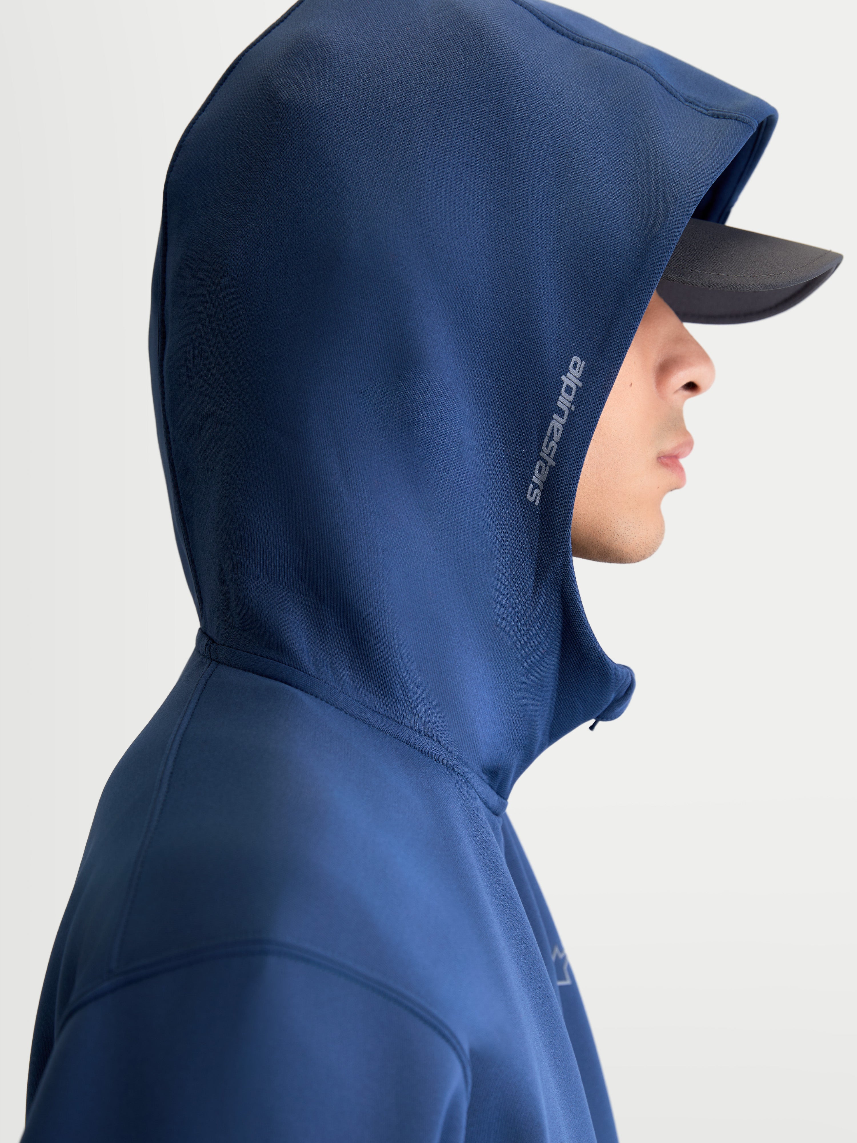 Alpinestars, bluza z kapturem Cypher, sportowa bluza polarowa z zamkiem z przodu, unisex, stalowoniebieska, wysoki kaptur z siatkową podszewką i bocznym logo Alpinestars, odzież sportowa inspirowana motorsportem, widok z profilu na modelu w czapce z daszkiem.