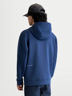 Alpinestars Bluza z kapturem Cypher, stalowoniebieska sportowa bluza z polarem, widok z tyłu na modelu prezentujący wysoki kaptur z siatkową podszewką oraz dyskretne logo Alpinestars na dole pleców, materiał tri-blend, casualowy styl motorsport.