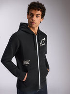 Bluza z kapturem Alpinestars Transverse, odzież sportowa typu casual, czarna z białym detalem zamka, kaptur ze sznurkami, logo gwiazdy Alpinestars na piersi, grafika „One Goal One Vision”, męski model z ciemnymi, kręconymi włosami
