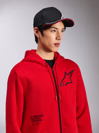 Bluza z kapturem Alpinestars Transverse, czerwony polar zapinany na zamek, czarne logo Astars na piersi i napis „One Goal. One Vision.” na dole z przodu, casualowa odzież streetwearowa, model w czarnej czapce z daszkiem