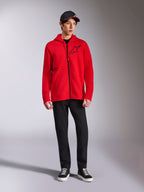 Alpinestars Transverse Hoodie, czerwona bluza polarowa zapinana na pełny zamek, czarne logo Astars na piersi i nadruk One Goal z boku, noszona przez modela z czarnymi spodniami i czapką, casualowy streetwear inspirowany sportami motorowymi
