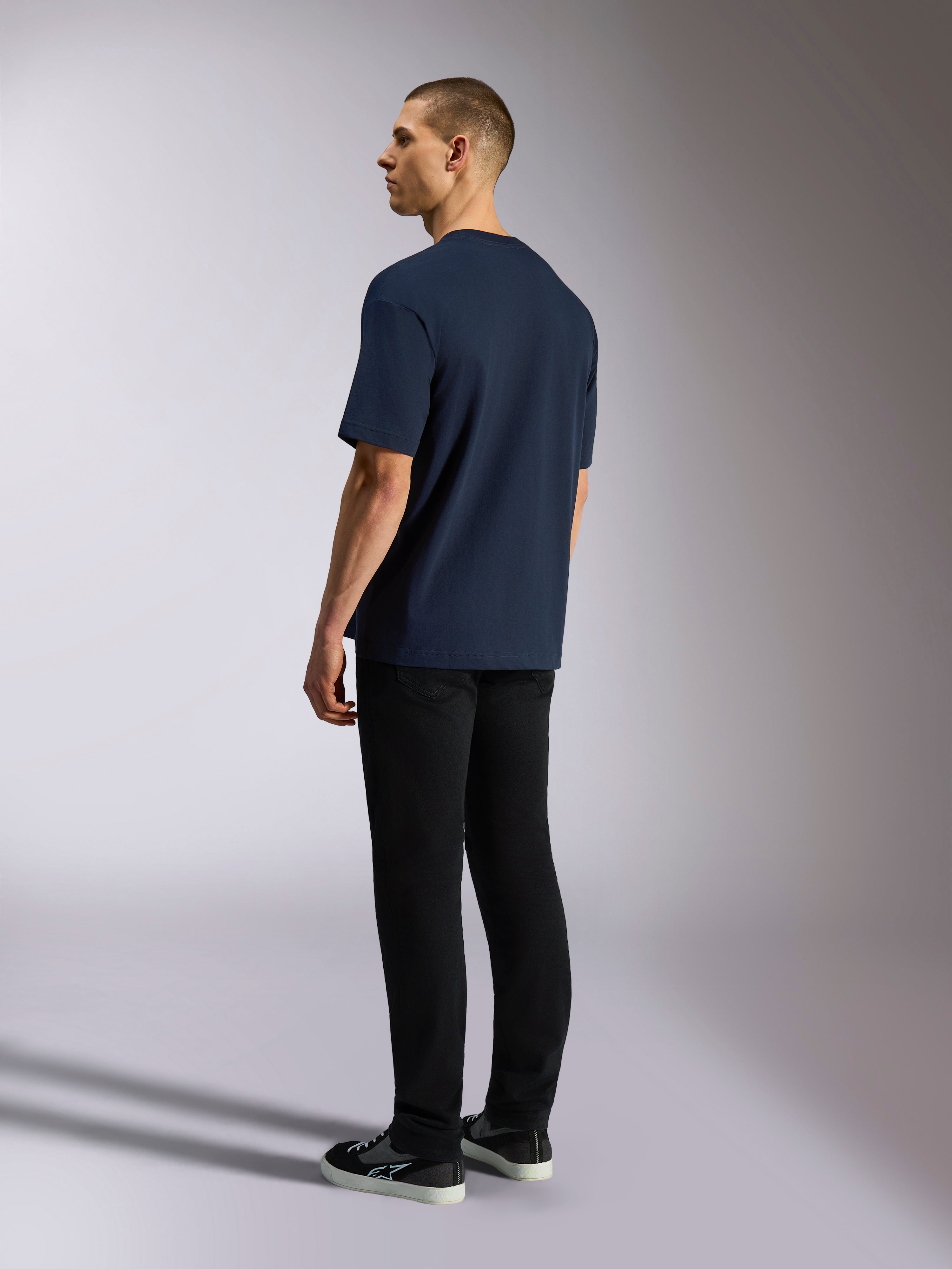Alpinestars Aplomb Oversized CSF Tee, koszulka z krótkim rękawem, granatowa, widok z tyłu na modelu, zestawiona z czarnymi spodniami i sneakersami, casualowy streetwear inspirowany sportami motorowymi
