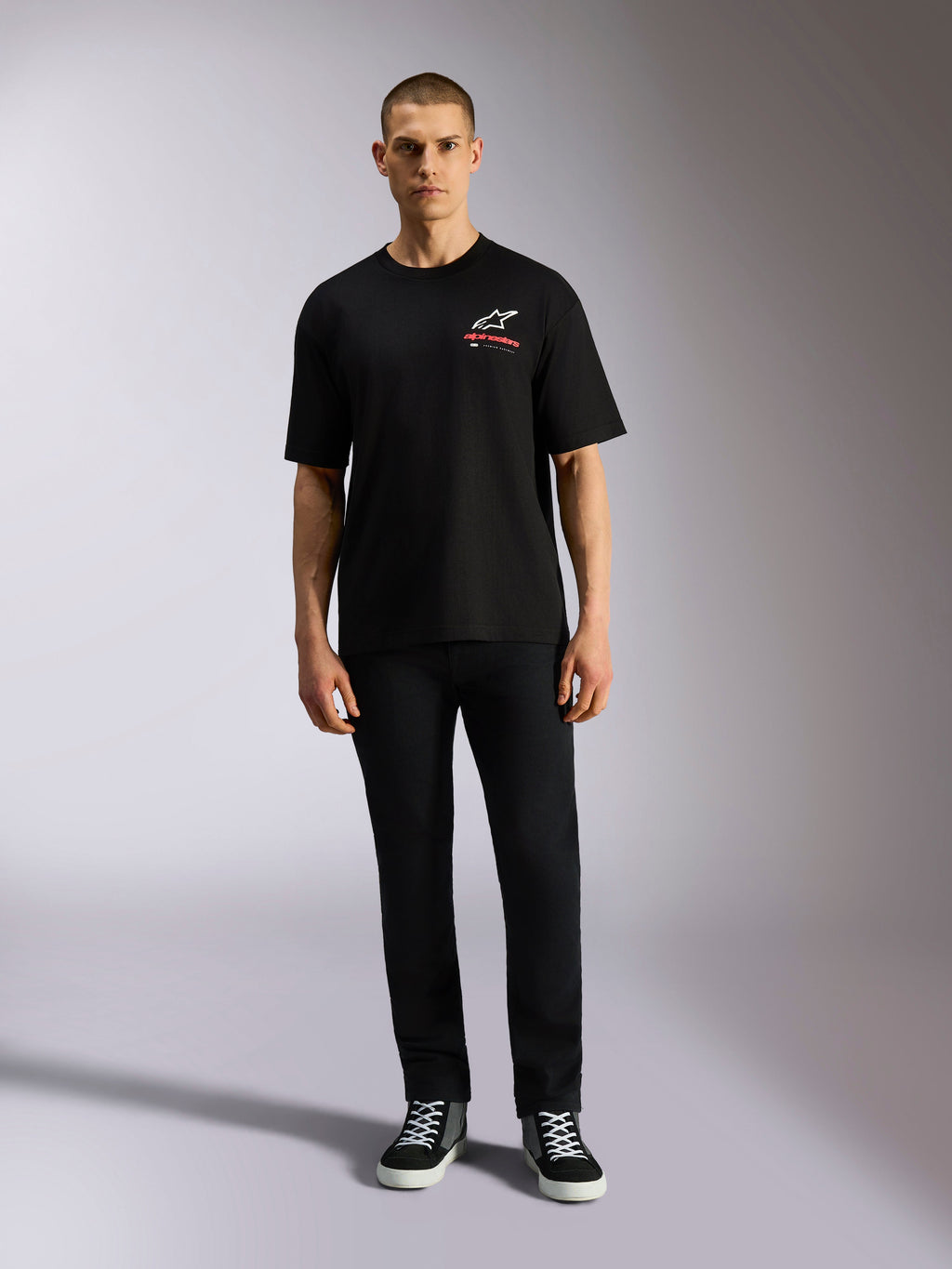 Alpinestars Overhang Oversized CSF Tee, koszulka z krótkim rękawem, czarna, białe logo Astars z czerwonym napisem, model w czarnych spodniach i butach sportowych, casualowy styl motorsportowy