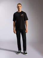 Alpinestars Overhang Oversized CSF Tee, koszulka z krótkim rękawem, czarna, białe logo Astars z czerwonym napisem, model w czarnych spodniach i butach sportowych, casualowy styl motorsportowy
