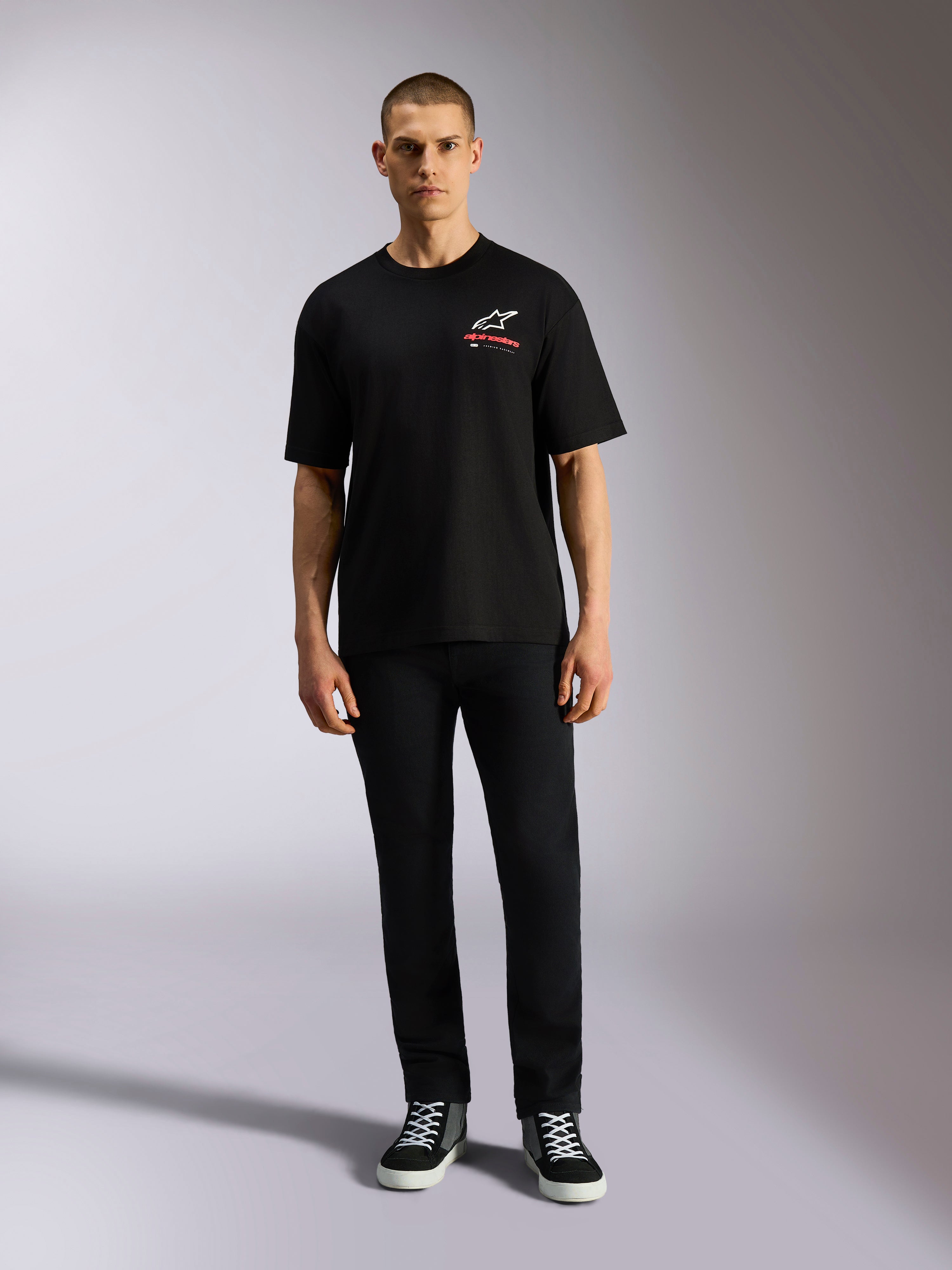 Alpinestars Overhang Oversized CSF Tee, koszulka z krótkim rękawem, czarna, białe logo Astars z czerwonym napisem, model w czarnych spodniach i butach sportowych, casualowy styl motorsportowy