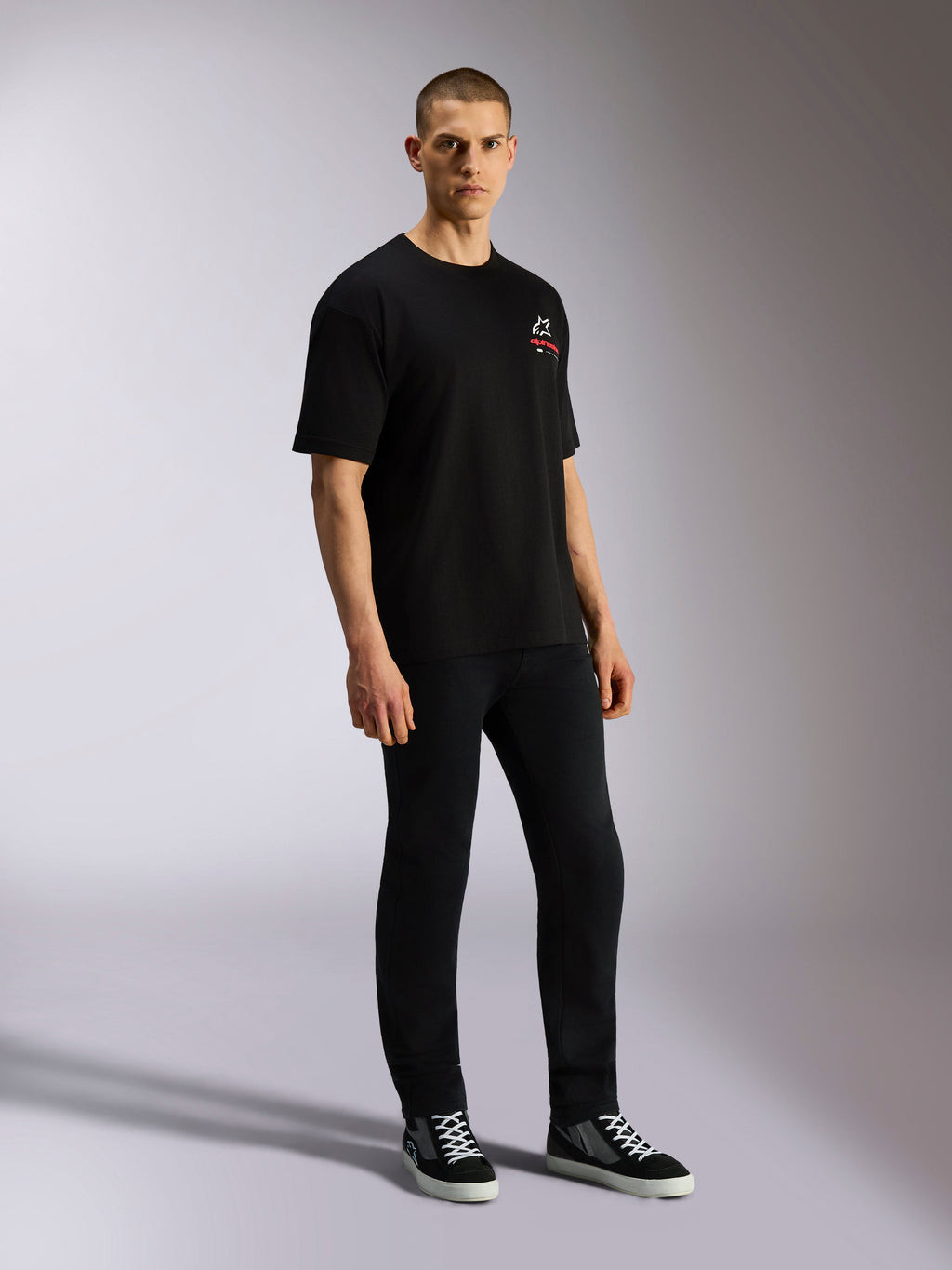 Alpinestars Overhang Oversized CSF Tee, czarny t-shirt z krótkim rękawem, biało-czerwone logo Astars z przodu, prezentowany przez modela w czarnych spodniach i sneakersach, luźny fason typu oversized w stylu streetwear