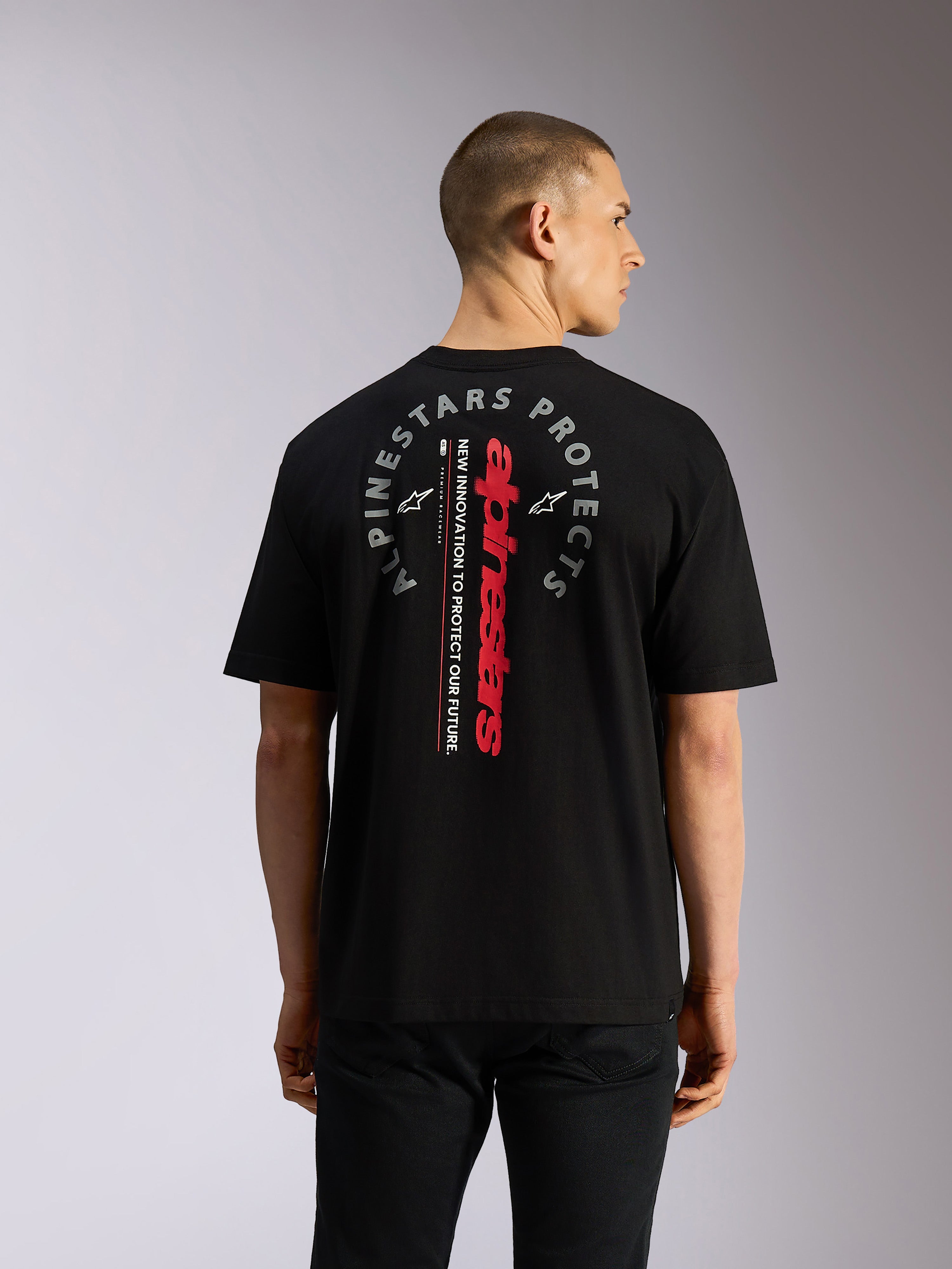 Alpinestars Overhang Oversized CSF Tee, koszulka z krótkim rękawem, czarna, widok z tyłu z pionowym czerwonym napisem Alpinestars i okrągłą szarą grafiką „Alpinestars Protects”, codzienna odzież uliczna inspirowana motorsportem