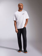 Alpinestars Wild Oversized CSF Tee, koszulka z krótkim rękawem, biała, żywe wielokolorowe logo Astars na piersi, zestawiona z czarnymi spodniami i sneakersami, codzienna odzież lifestyle w stylu motorsport
