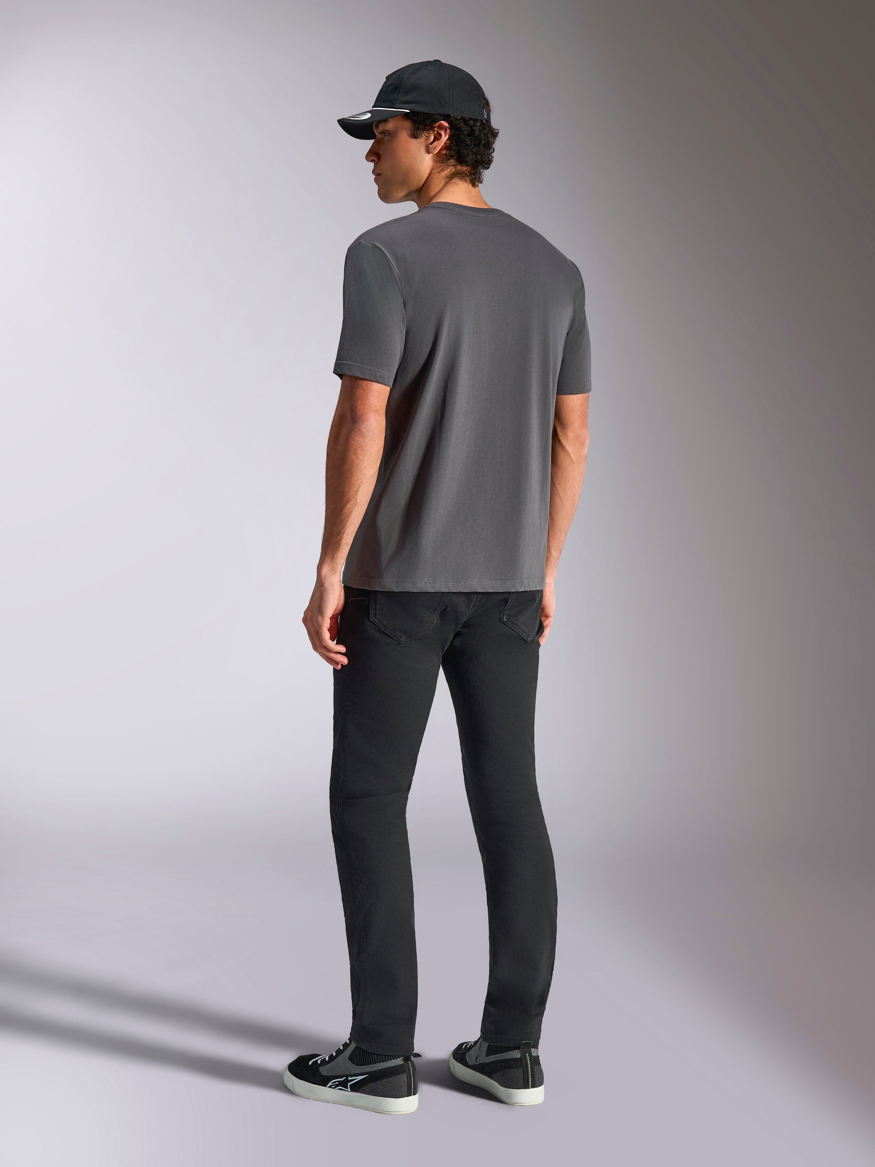 Alpinestars Ellipsoid CSF Tee, koszulka z krótkim rękawem, ciemnoszary grafit, widok z tyłu, model w czarnych spodniach i czarnej czapce z daszkiem, codzienna odzież uliczna w stylu motorsportowym