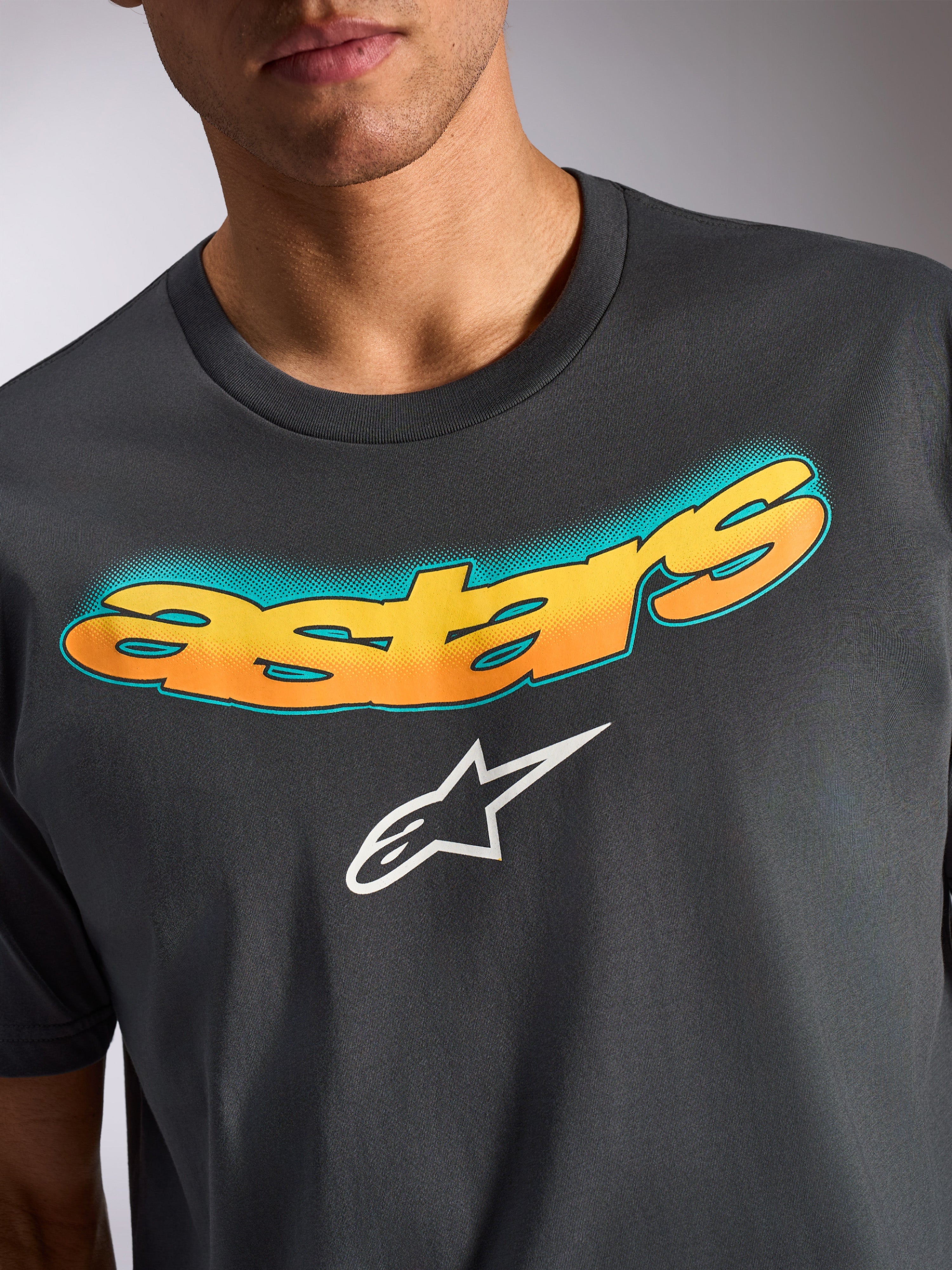 Alpinestars Ellipsoid CSF Tee, koszulka z krótkim rękawem, grafitowa, zakrzywiony napis „astars” z żółto-pomarańczowym gradientem i turkusowym wzorem w kropki, białe logo gwiazdy Alpinestars, codzienna odzież inspirowana sportami motorowymi