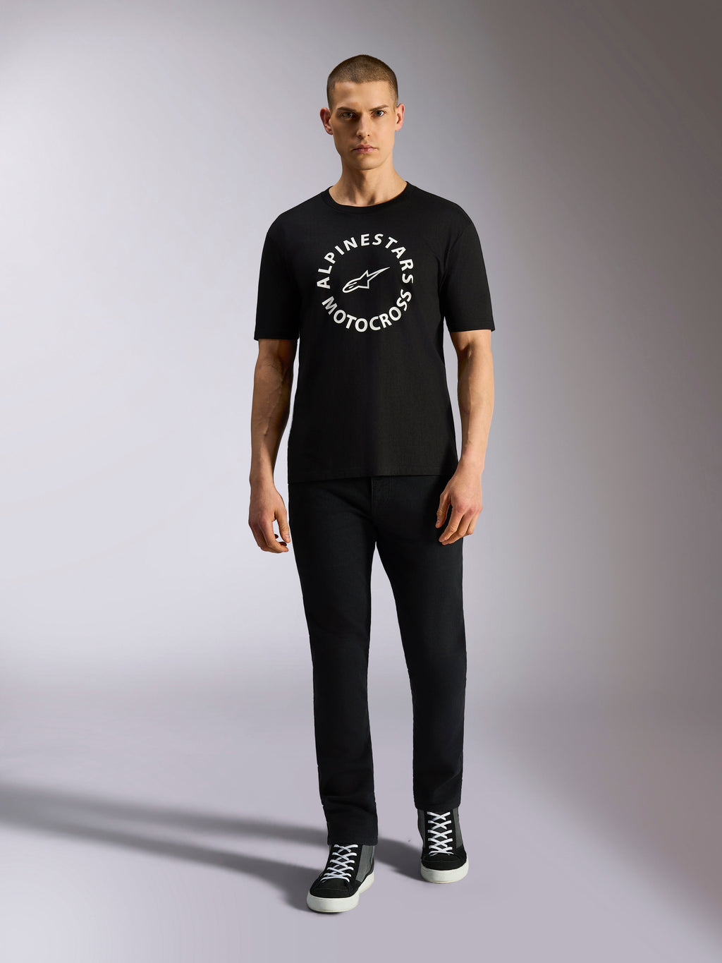 Alpinestars MX CSF Tee, koszulka z krótkim rękawem, czarna, biała okrągła grafika Alpinestars Motocross, prezentowana przez modela w czarnych spodniach i sneakersach, casualowa odzież motorsport streetwear
