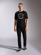 Alpinestars MX CSF Tee, koszulka z krótkim rękawem, czarna, biała okrągła grafika Alpinestars Motocross, prezentowana przez modela w czarnych spodniach i sneakersach, casualowa odzież motorsport streetwear