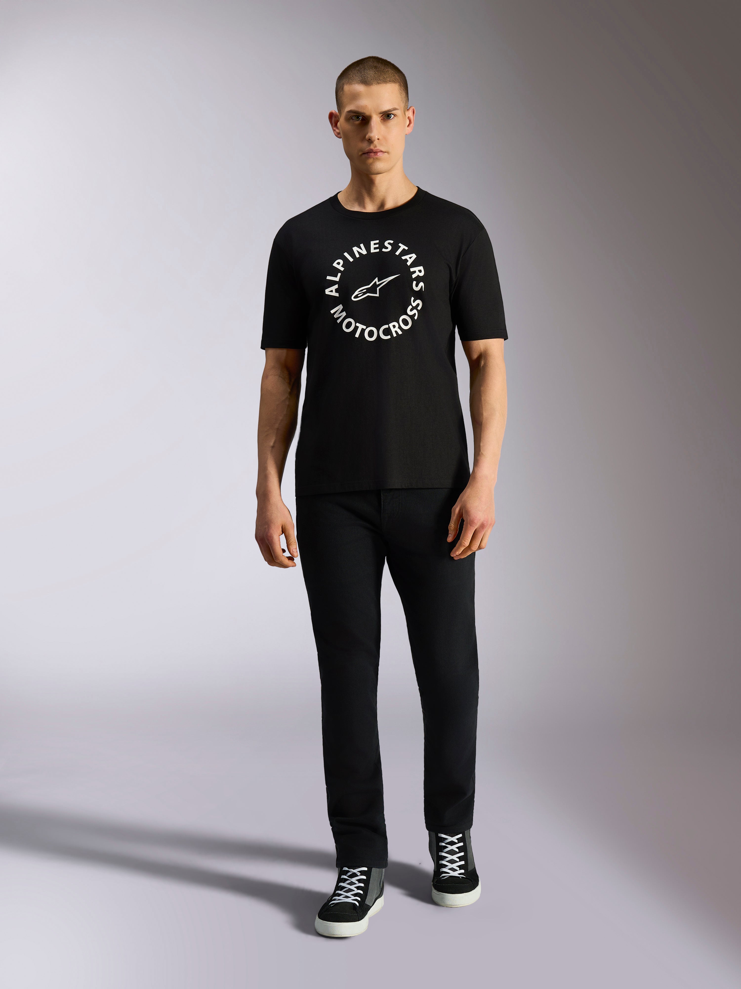 Alpinestars MX CSF Tee, koszulka z krótkim rękawem, czarna, biała okrągła grafika Alpinestars Motocross, prezentowana przez modela w czarnych spodniach i sneakersach, casualowa odzież motorsport streetwear