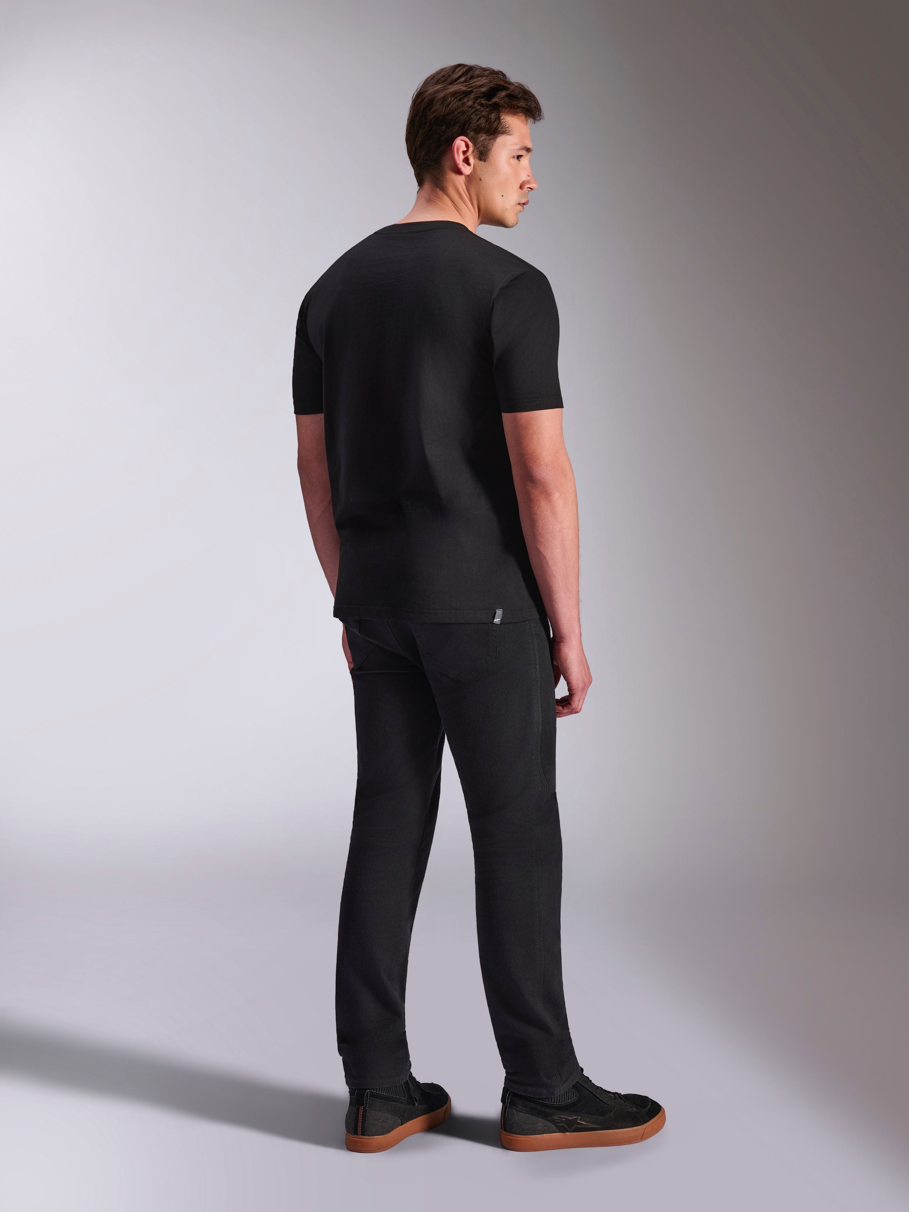 Alpinestars Abus CSF Tee, koszulka z krótkim rękawem, czarna, widok z tyłu na modelu, casualowy streetwear w stylu motorsport, zestawiona z ciemnymi spodniami i sneakersami