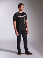 Alpinestars Abus CSF Tee, koszulka z krótkim rękawem, czarna, z zakrzywionym czerwono-białym logo Alpinestars i pionowo ułożonymi grafikami, noszona z czarnymi spodniami i sneakersami, casualowa odzież uliczna inspirowana motorsportem
