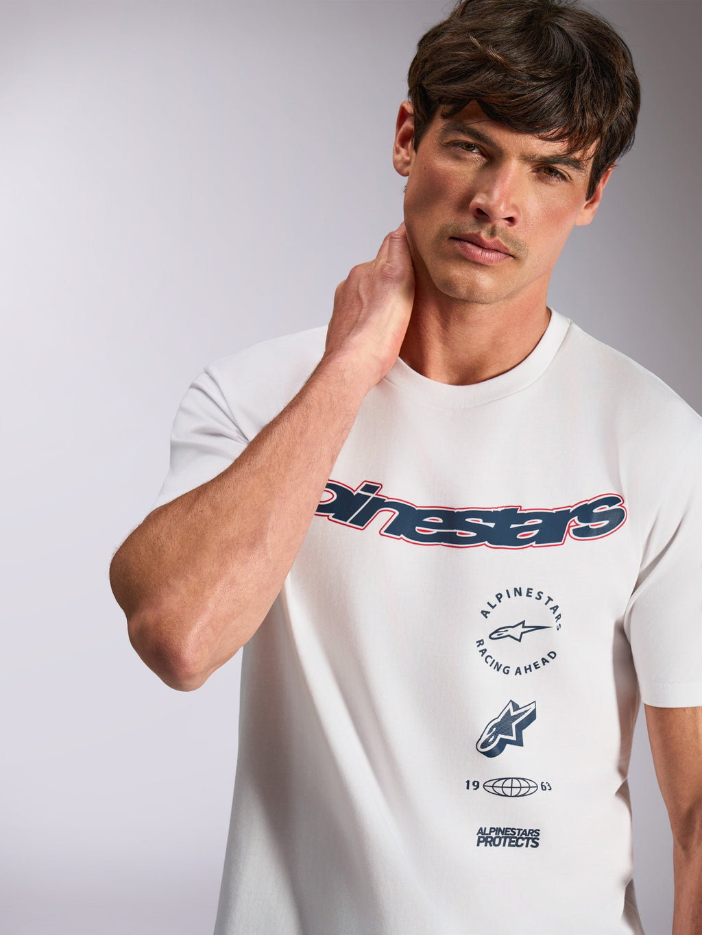 Alpinestars Abus CSF Tee, biała koszulka z krótkim rękawem, granatowe zakrzywione logo Alpinestars z czerwoną obwódką, wielowarstwowe grafiki, casualowa odzież uliczna w stylu motorsportowym