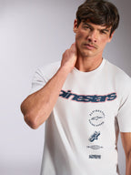 Alpinestars Abus CSF Tee, biała koszulka z krótkim rękawem, granatowe zakrzywione logo Alpinestars z czerwoną obwódką, wielowarstwowe grafiki, casualowa odzież uliczna w stylu motorsportowym
