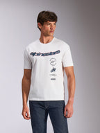 Alpinestars Abus CSF Tee, koszulka z krótkim rękawem, biała, zakrzywione logo Alpinestars z wielowarstwowymi grafikami na klatce piersiowej, model w ciemnych jeansach, casualowa odzież uliczna w stylu motorsport