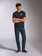 Alpinestars Angler CSF Tee, czarna koszulka z krótkim rękawem, żywe wielokolorowe logo Astars na piersi, model ze skrzyżowanymi ramionami, ciemne dżinsy i czarne sneakersy, casualowa odzież motorsportowa