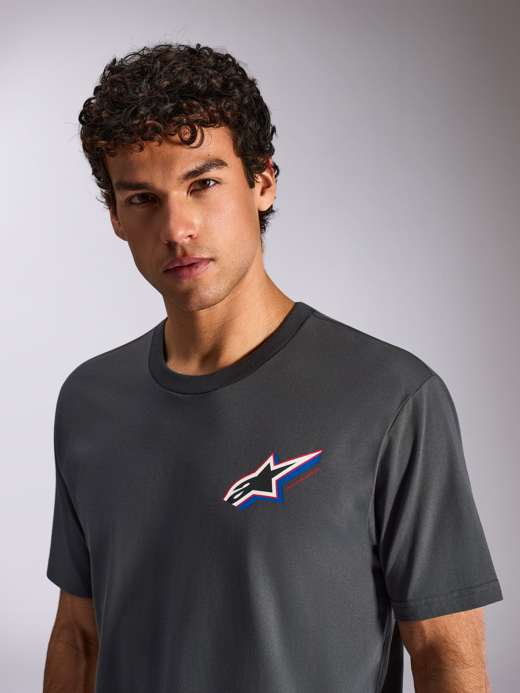 Alpinestars Angler CSF Tee, koszulka z krótkim rękawem, ciemnoszara, noszona przez modela, z wielokolorowym logo Astars na piersi, casualowy streetwear motorsportowy