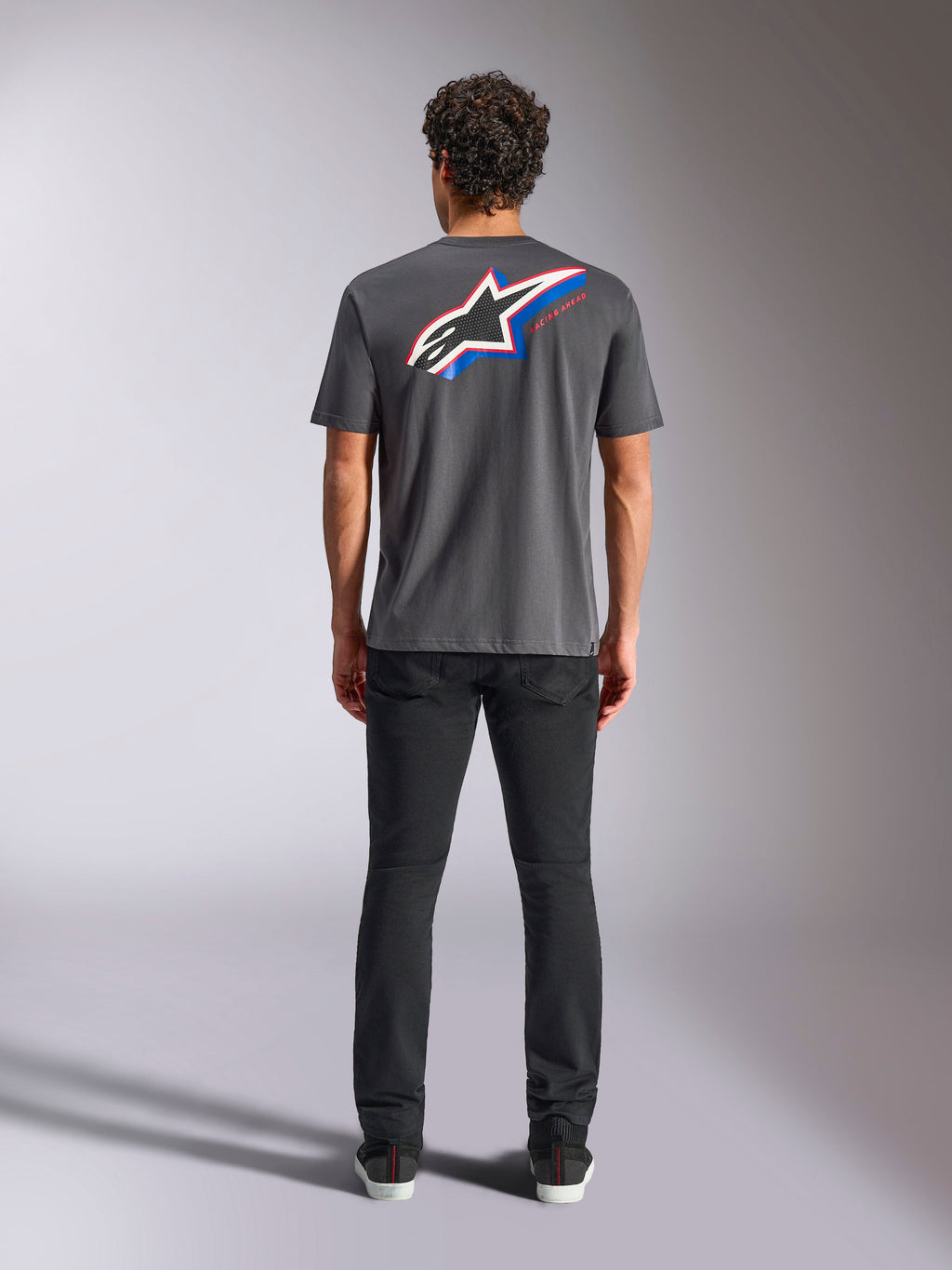 Koszulka Alpinestars Angler CSF, T-shirt z krótkim rękawem, grafitowy, duże wielokolorowe logo Astars na plecach z czerwonymi i niebieskimi akcentami, widok z tyłu na modelu, codzienna odzież streetwearowa w stylu motorsport